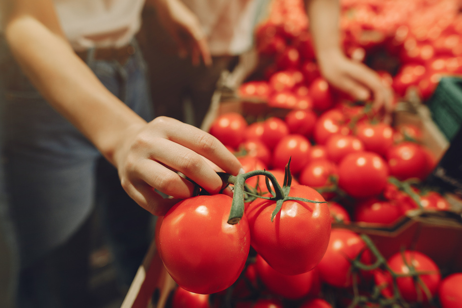 Crop woman choosing ripe tomatoes in grocery store